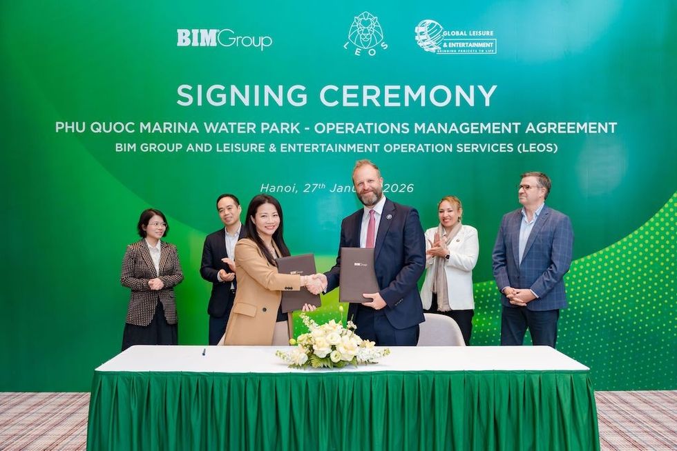 People shaking hands at a signing ceremony with green backdrop.