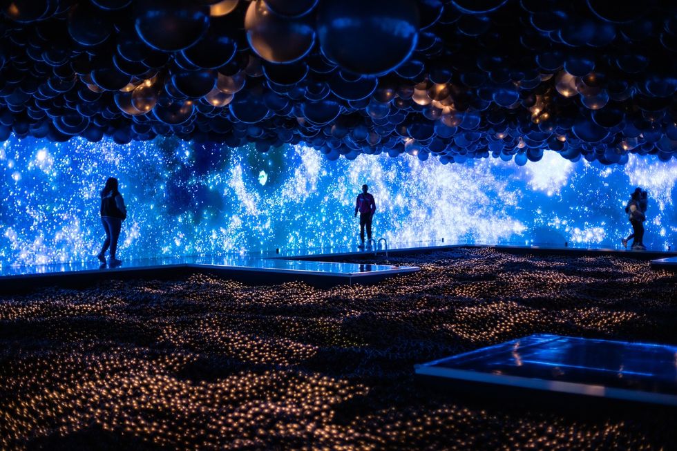 People silhouetted against a blue starry wall installation with a dark, textured foreground, Balloon Museum