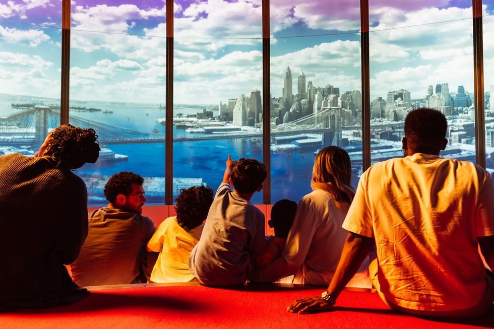 People sitting and pointing at a city skyline viewed through large panoramic windows in the Times Travel experience.