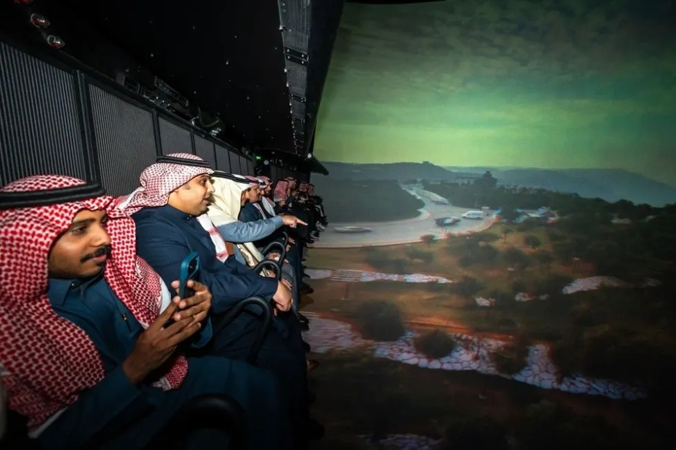 People sitting on a simulator flying theatre ride, Flying Over Saudi, with a landscape scene projected ahead.