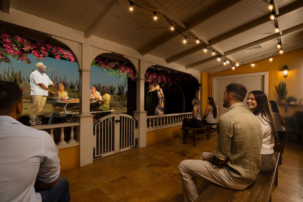 People sitting on benches, watching a vibrant, lit-up dining scene on a decorated patio.