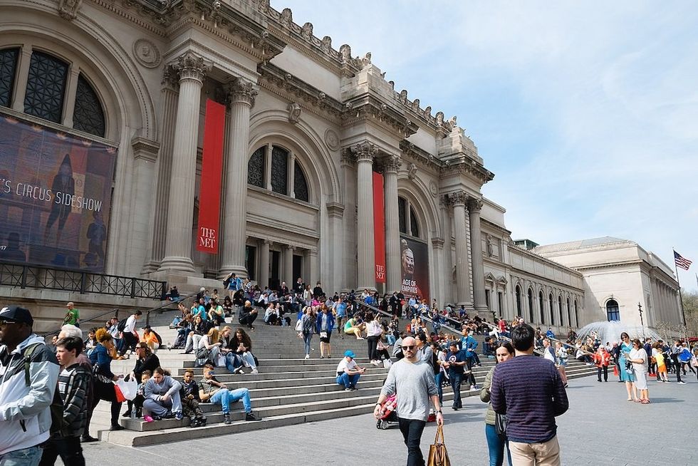 People sitting on steps of a grand building, The Metropolitan Museum of Art, with large columns and banners.