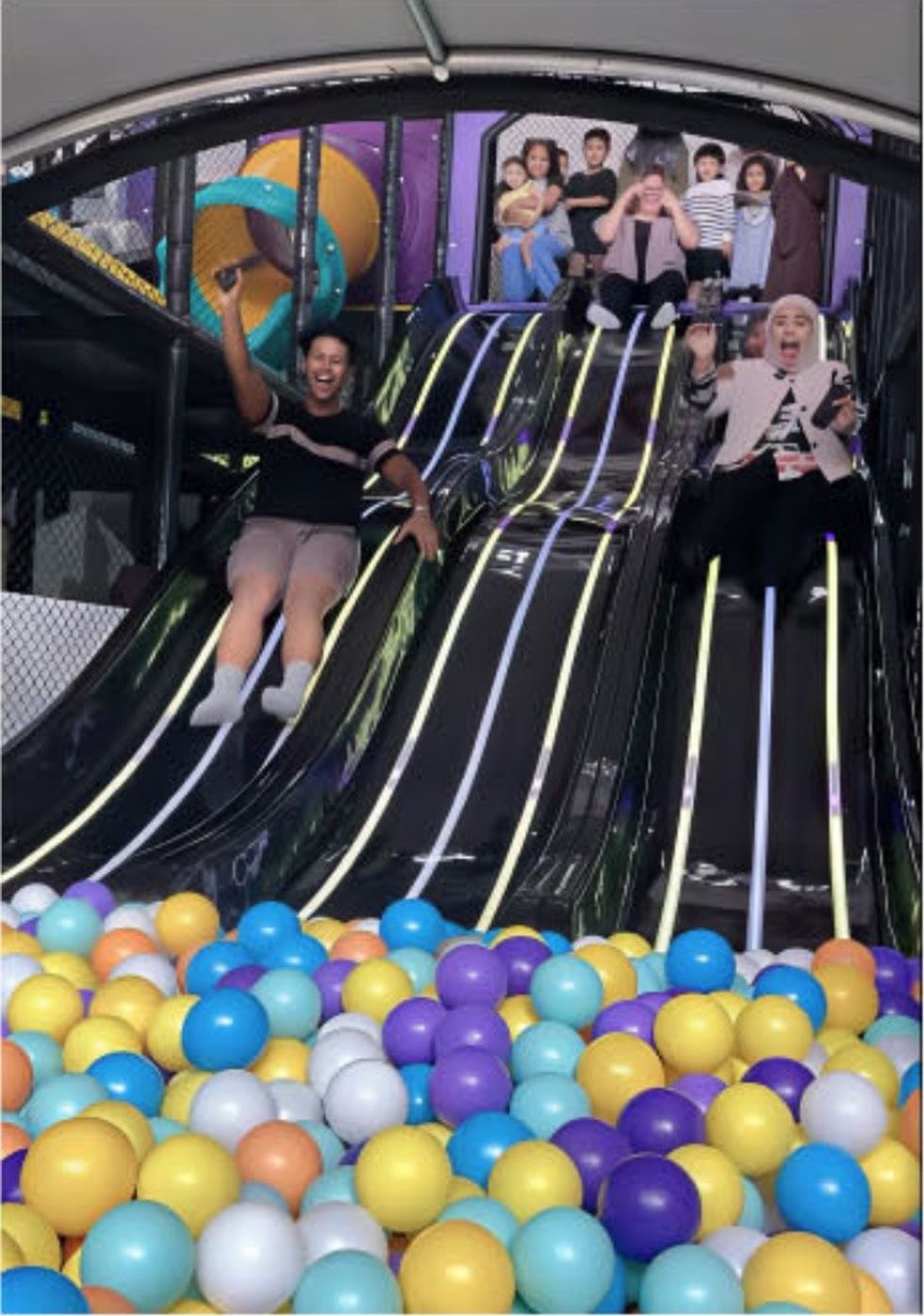 People sliding into a colorful ball pit indoors, smiling and enjoying.