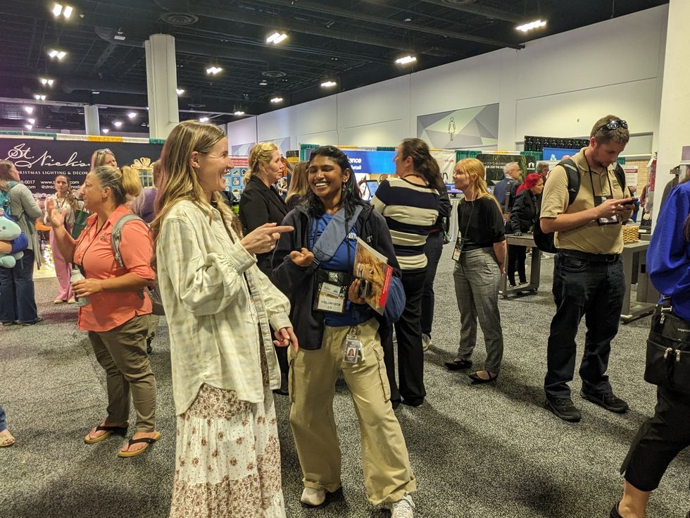 People socializing at a busy convention with booths in the background.