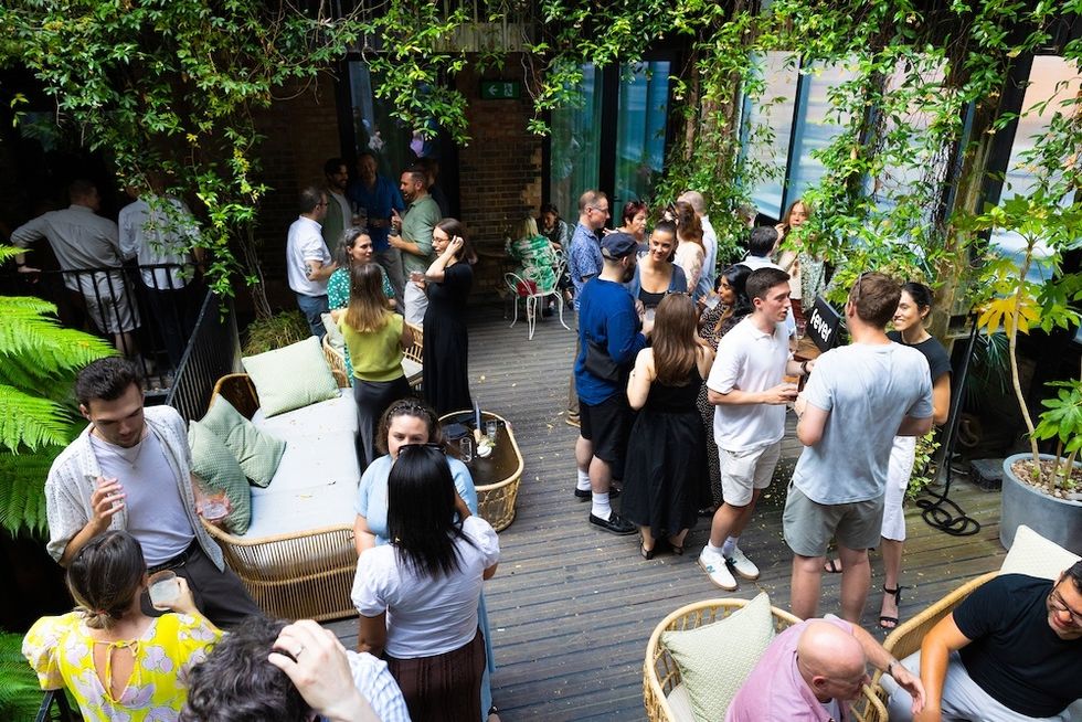 People socializing at a lively outdoor gathering with greenery and seating.