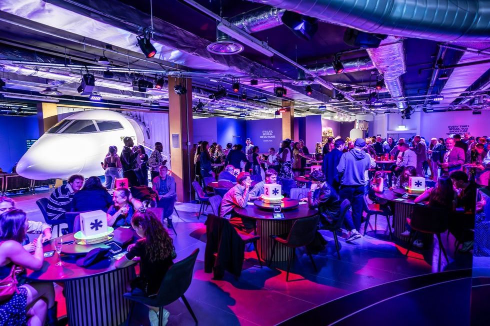 People socializing in a vibrant, airplane-themed venue with colorful lighting.