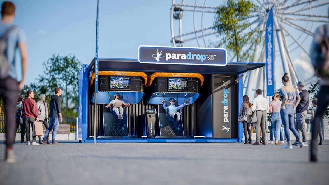 People trying VR paragliding at a "paradropVR" booth, with a Ferris wheel in the background.