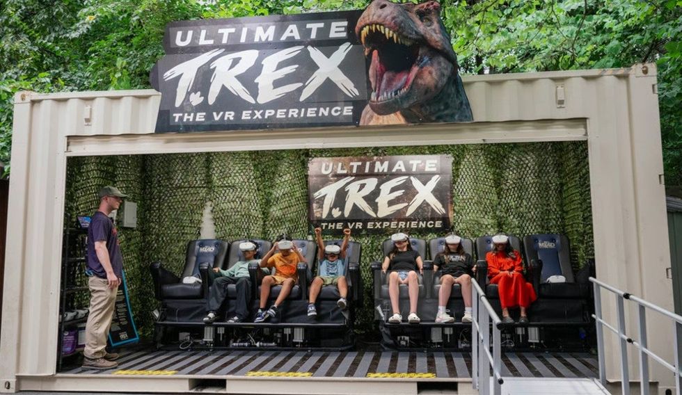 People using VR headsets for a T. Rex experience inside a camouflaged container setup.