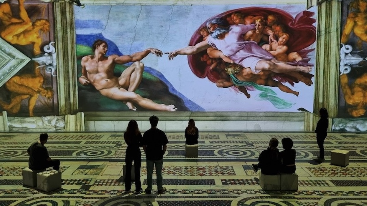 People view a digital projection of the Sistine Chapel's "Creation of Adam" on a large wall.