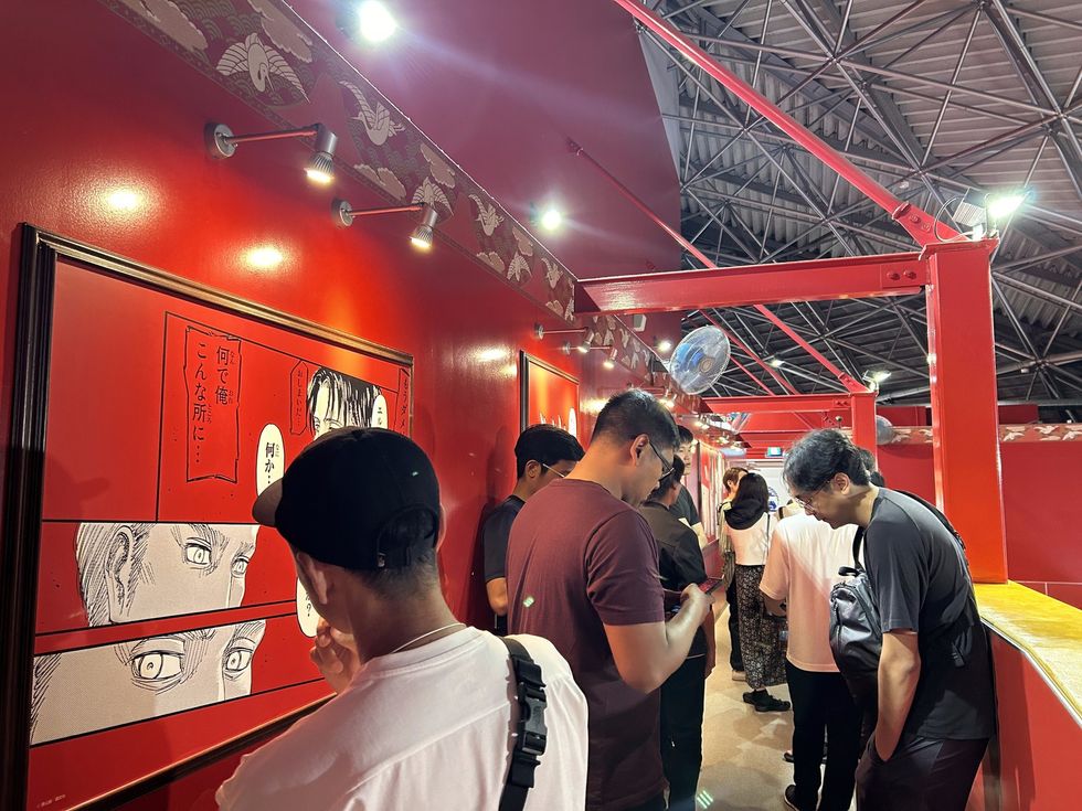 People view manga art panels on a red wall at an indoor exhibit.