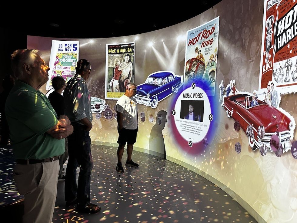People viewing a curved exhibit wall with vintage car posters.