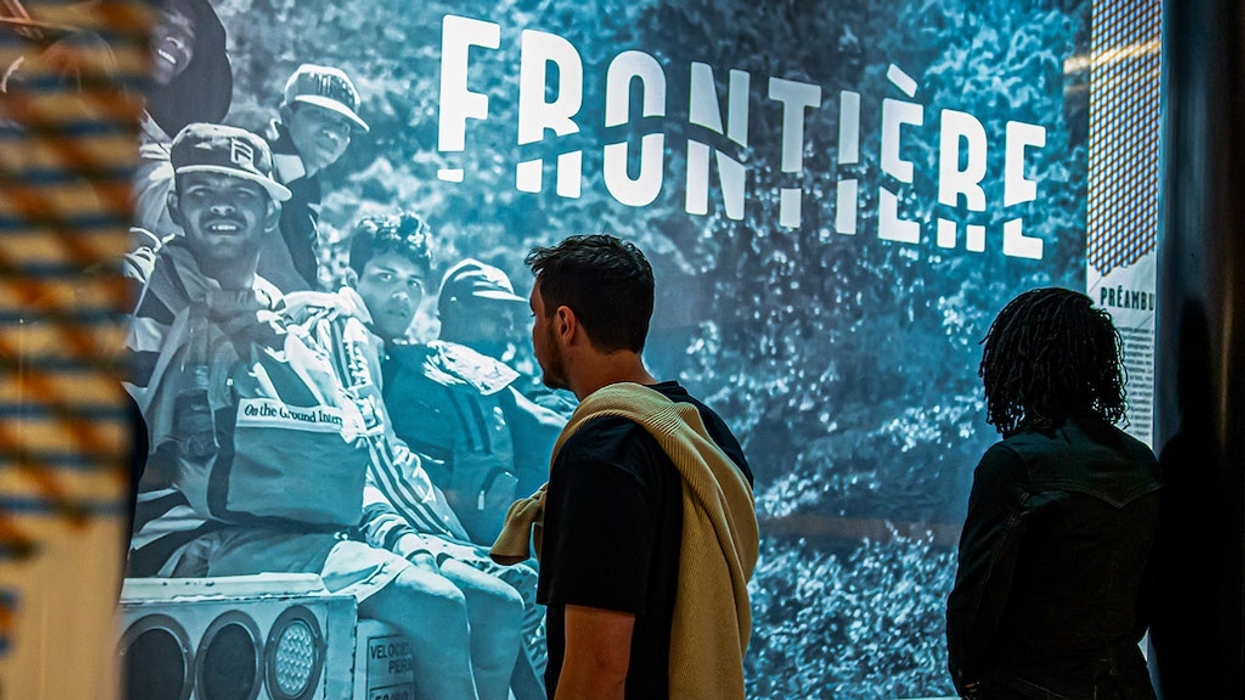 People viewing a large black-and-white mural titled "Frontière" in a dimly lit space.