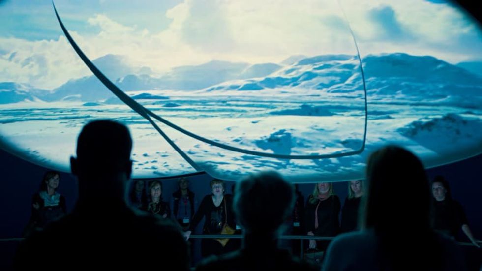 People viewing a large screen showing a snowy landscape under a curved dome.