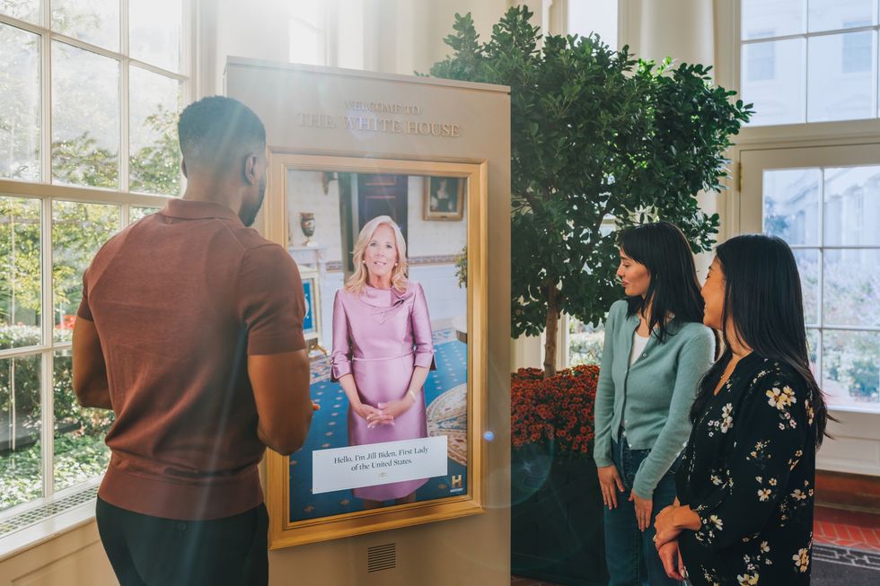 People viewing an interactive screen of the First Lady in a bright, plant-filled room - ESI