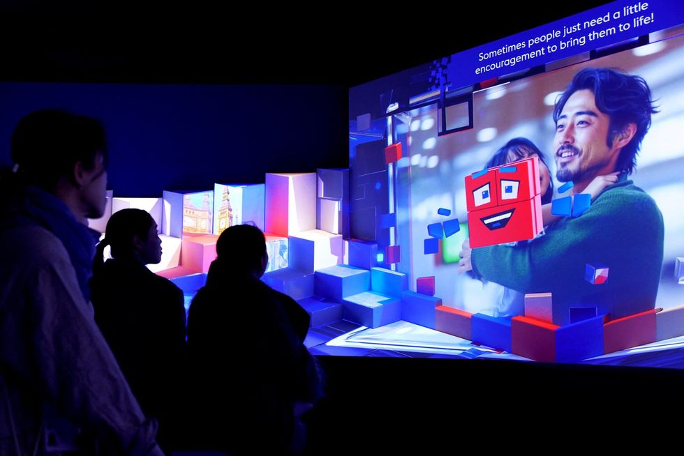 People viewing colorful digital display with smiling animated character and quote above.