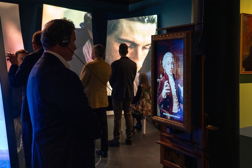 People viewing digital art exhibits in a dimly lit gallery with headphones.