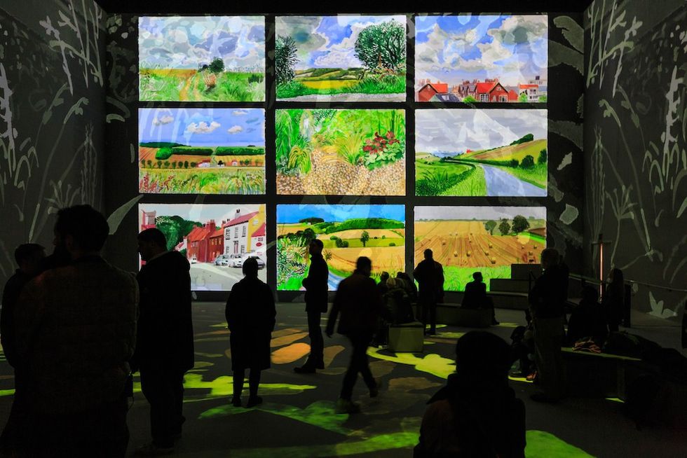 People viewing nine landscape David Hockney paintings projected on a large wall in a dark room at Lightroom