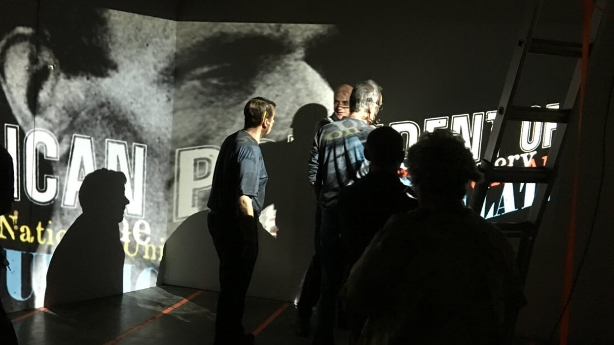 People viewing projected text and image on a dimly lit wall with a ladder on the side.