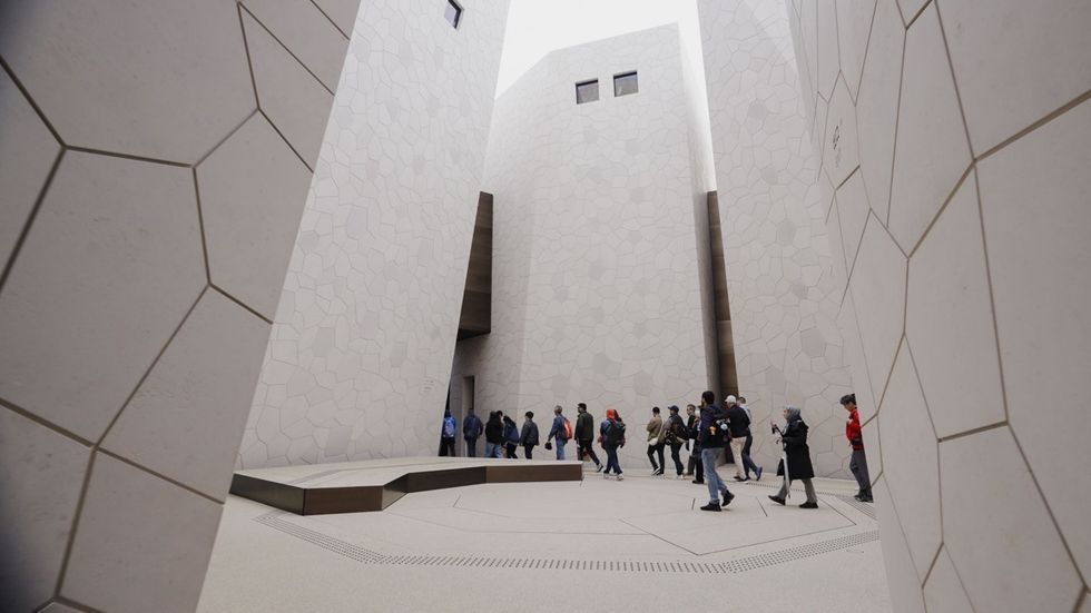 People walk through a courtyard surrounded by modern, geometric stone walls.