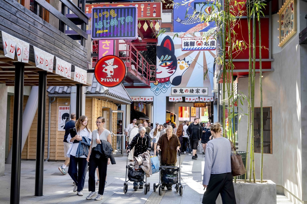 People walking in a colorful Japanese-themed street with vibrant signs and bamboo plants at Tivoli Gardens