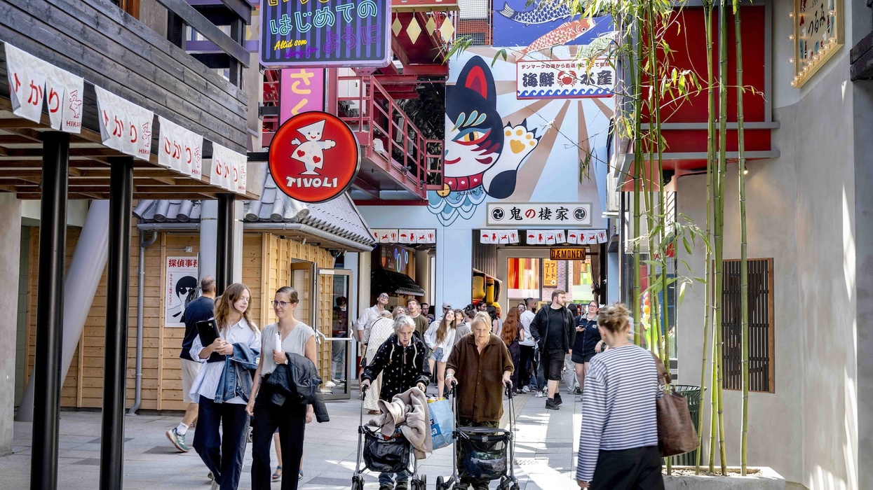 People walking in a colorful Japanese-themed street with vibrant signs and bamboo plants at Tivoli Gardens