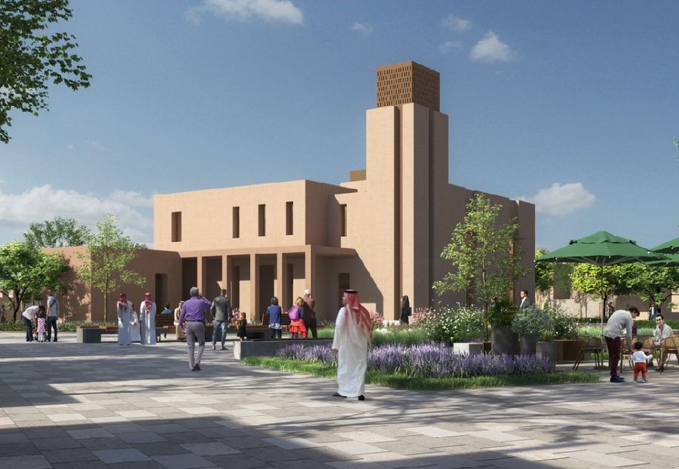 People walking in a sunny plaza at Roshn with a modern beige building and lush greenery