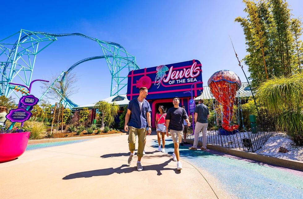 People walking outside SeaWorld San Diego \u2013 \u201cJewels of the Sea" entrance with roller coaster in the background.