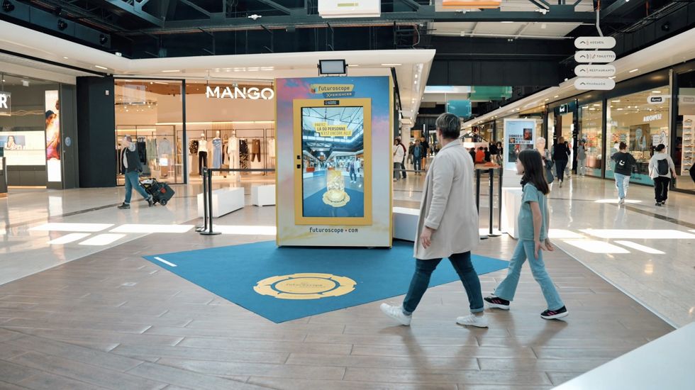 People walking past a digital kiosk in a busy shopping mall.
