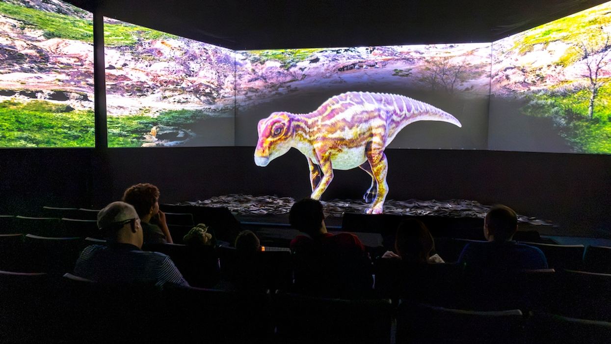 People watch a dinosaur hologram in a dark theater setting.