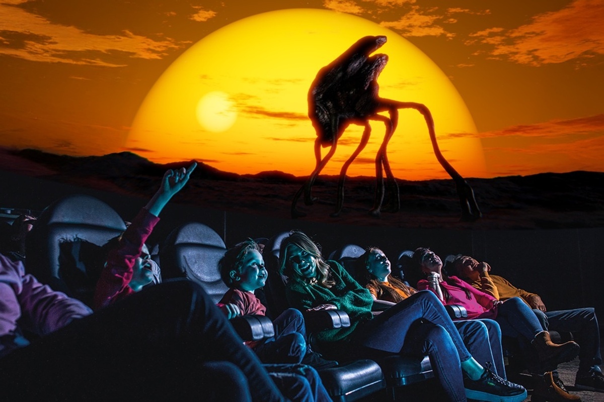 People watch a sunset with a surreal creature on a screen, sitting in theatre seats in the planetarium at Life.