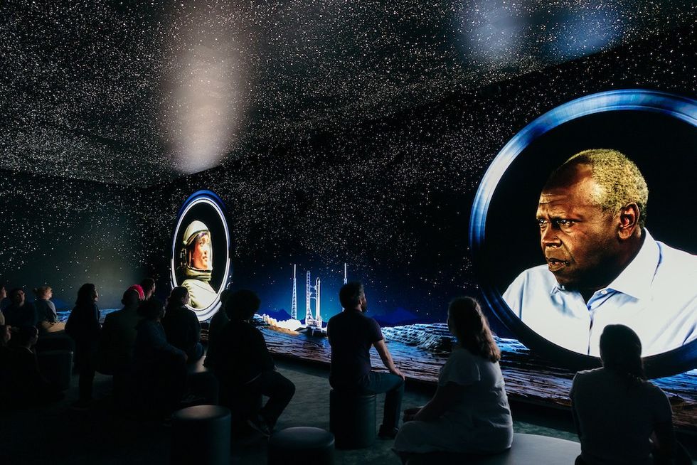 People watch projected images of an astronaut and man amid a starry backdrop.