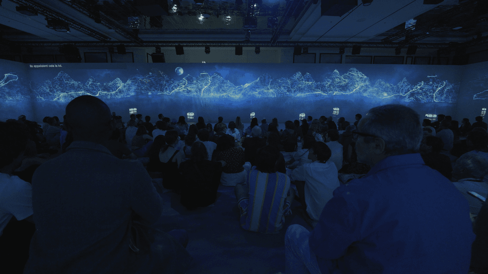 People watching a blue digital art display in a dimly lit room.