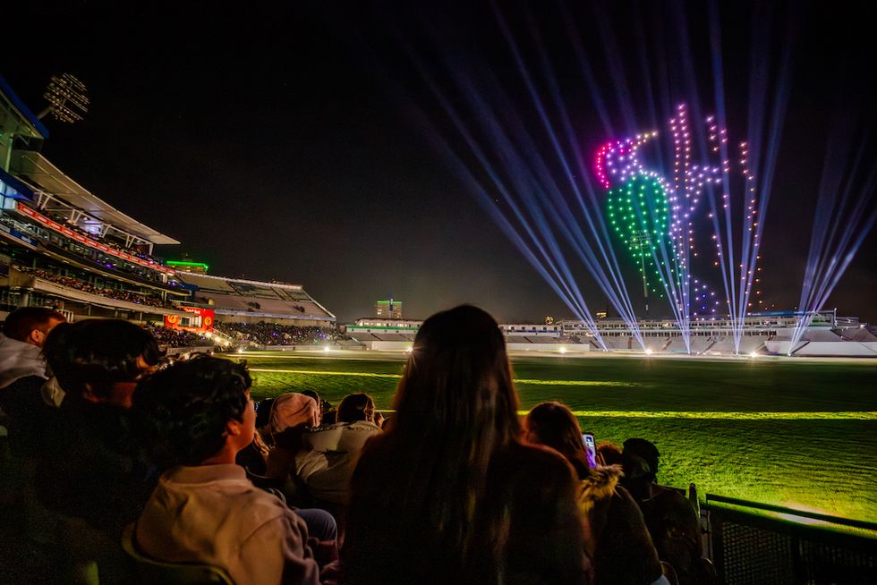 People watching a colorful drone light show at a stadium.