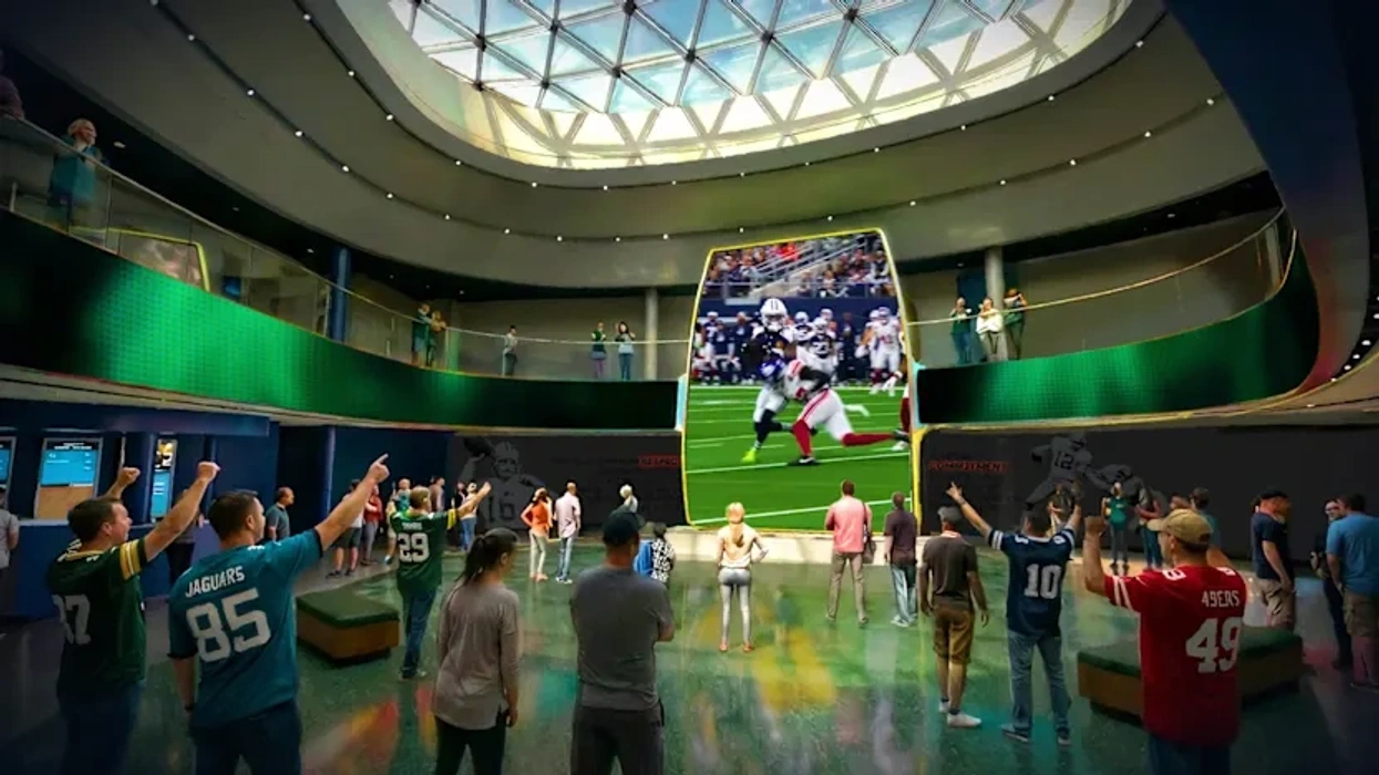 People watching a football game on a giant screen in an indoor stadium setting.