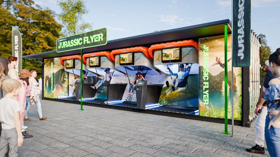 People watching a Jurassic Flyer flight simulator at an outdoor event.