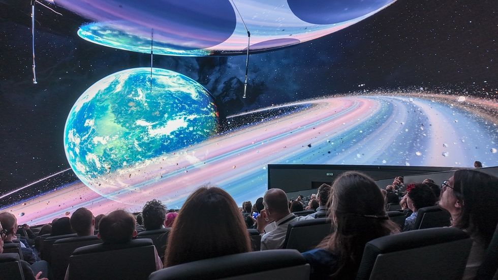 People watching a planetarium show in a Cosm dome, with colorful planets and rings displayed above.