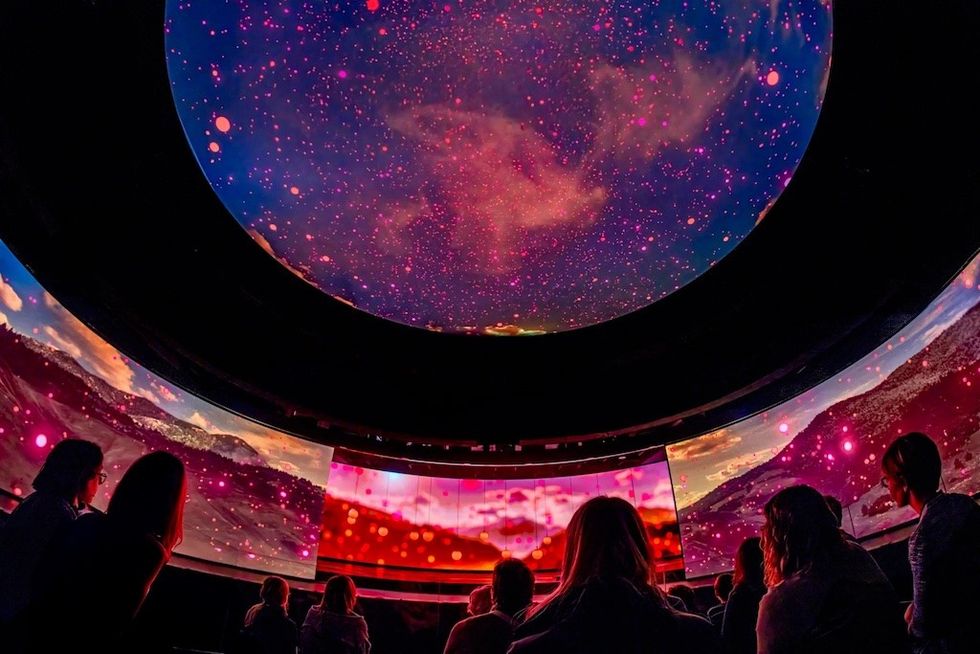 People watching pink-hued visuals in a dome-shaped planetarium.