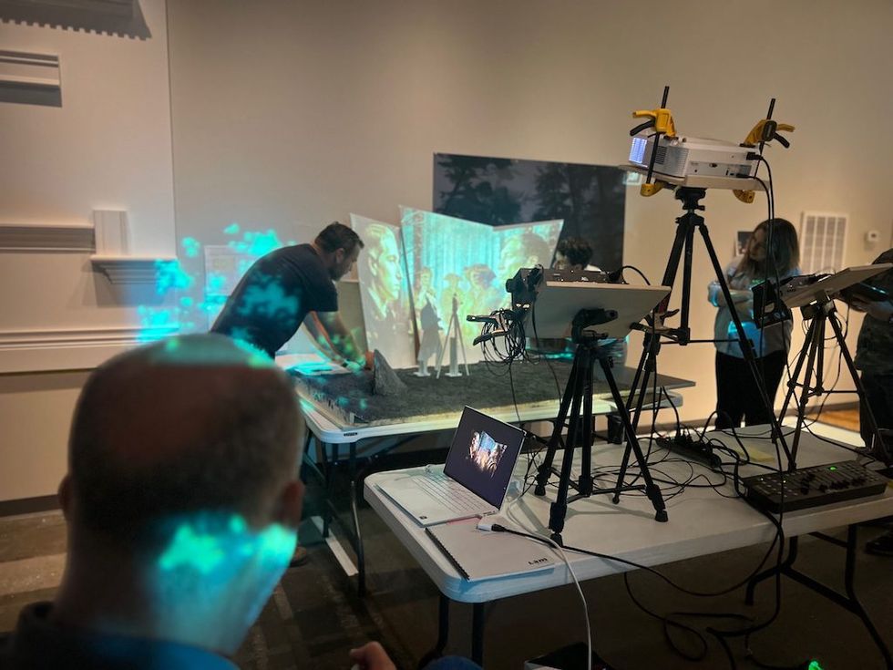 People working with projectors and screens on a table in a dimly lit room.