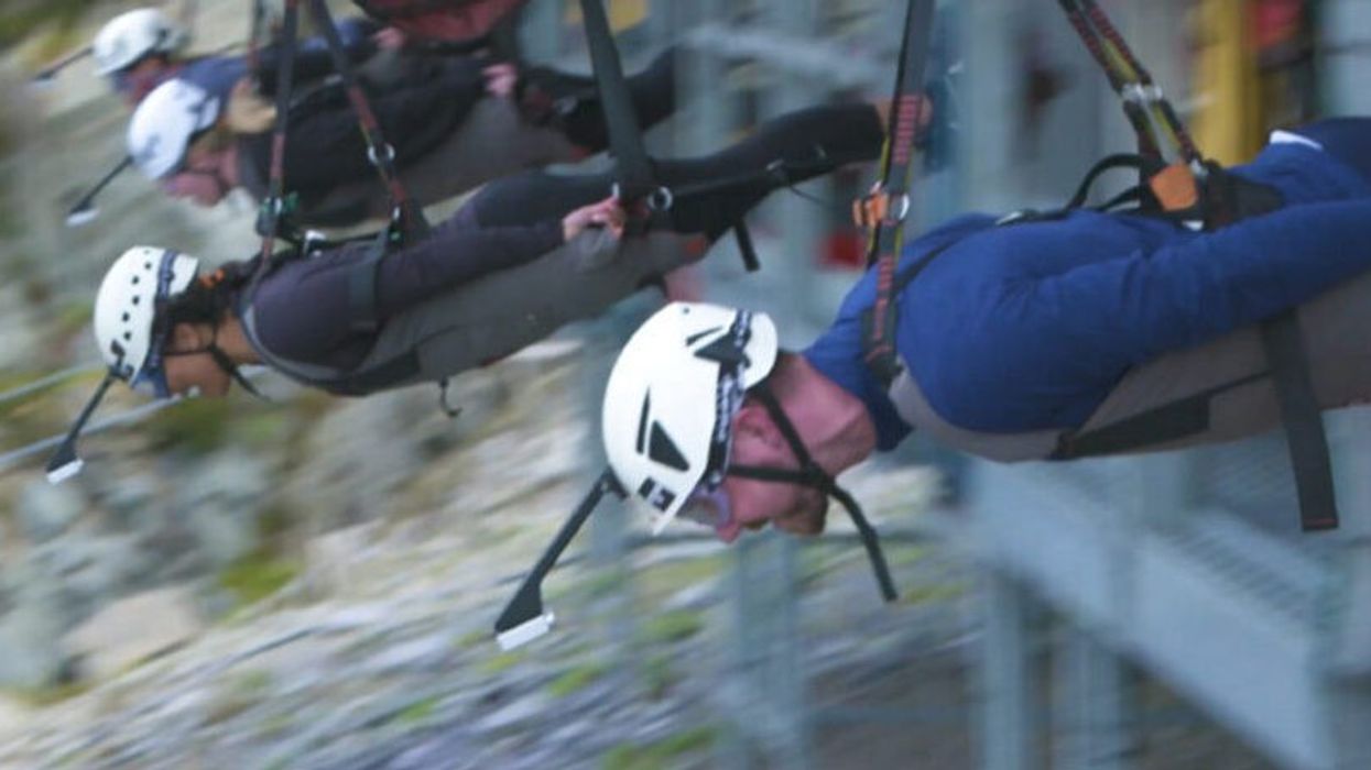 People zip-lining in a row, wearing helmets and harnesses.