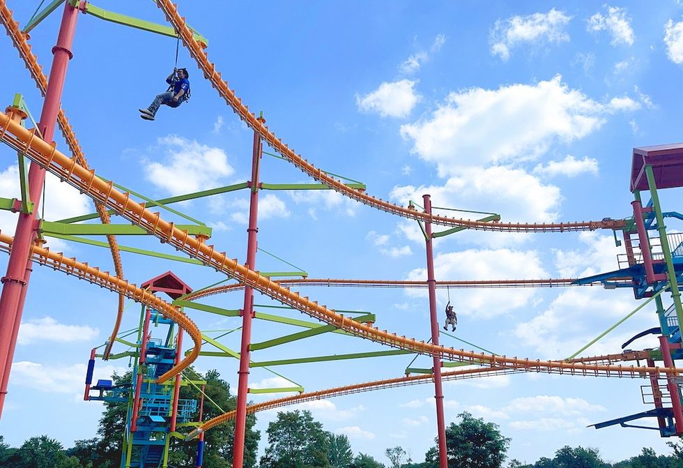 People ziplining on a colorful aerial course against a blue sky with clouds.