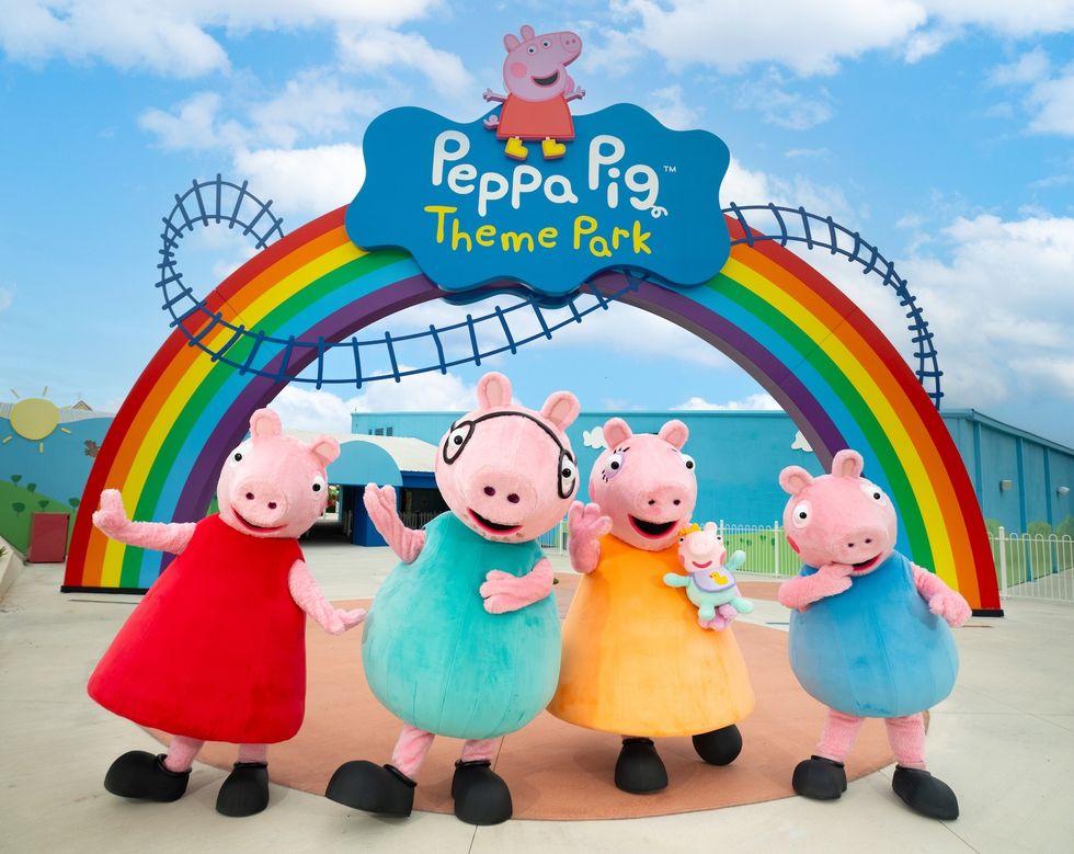 Peppa Pig characters in front of a rainbow arch at the theme park entrance.