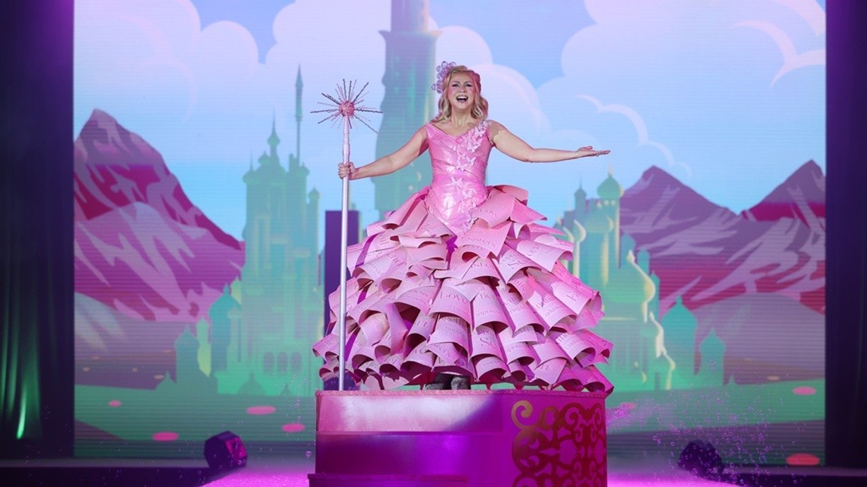 Performer in a pink dress onstage with a whimsical backdrop, holding a sparkling wand.