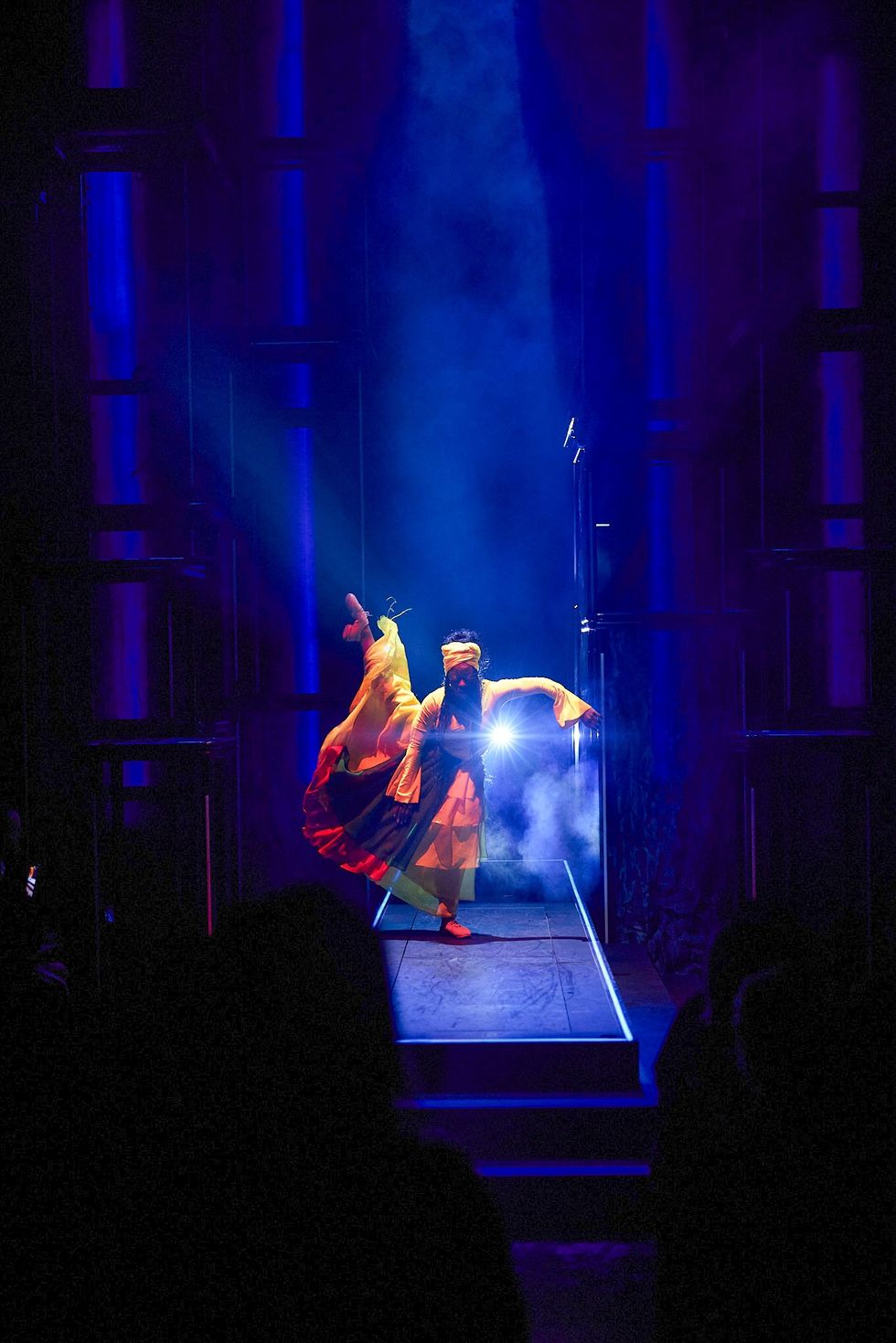 Performer in bright attire dances on stage with dramatic blue lighting and smoke.