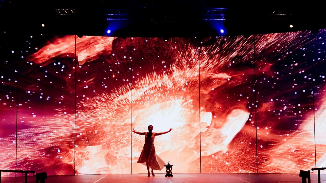 Performer on stage with vivid cosmic explosion backdrop under blue lights.