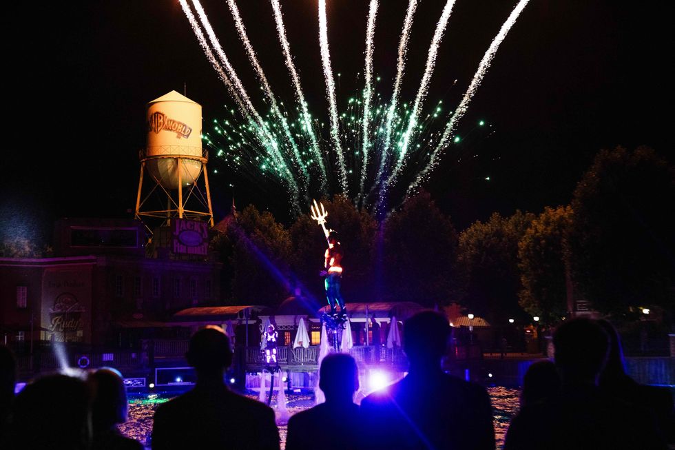 Performer on water jetpack with fireworks overhead and spectators watching at night.