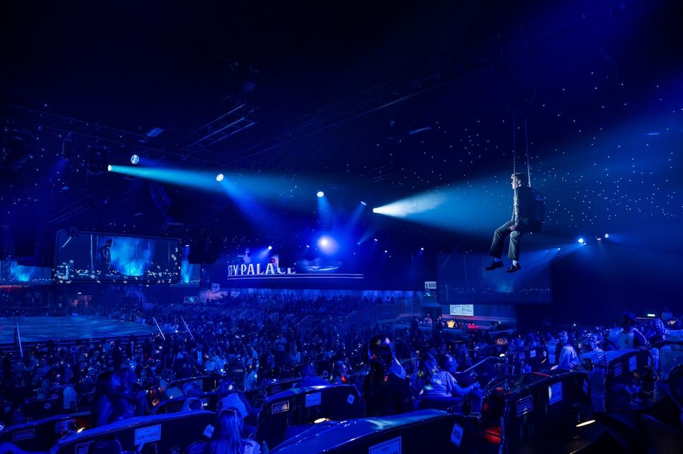 Performer suspended over a blue-lit crowd in a large, starry-ceilinged venue.