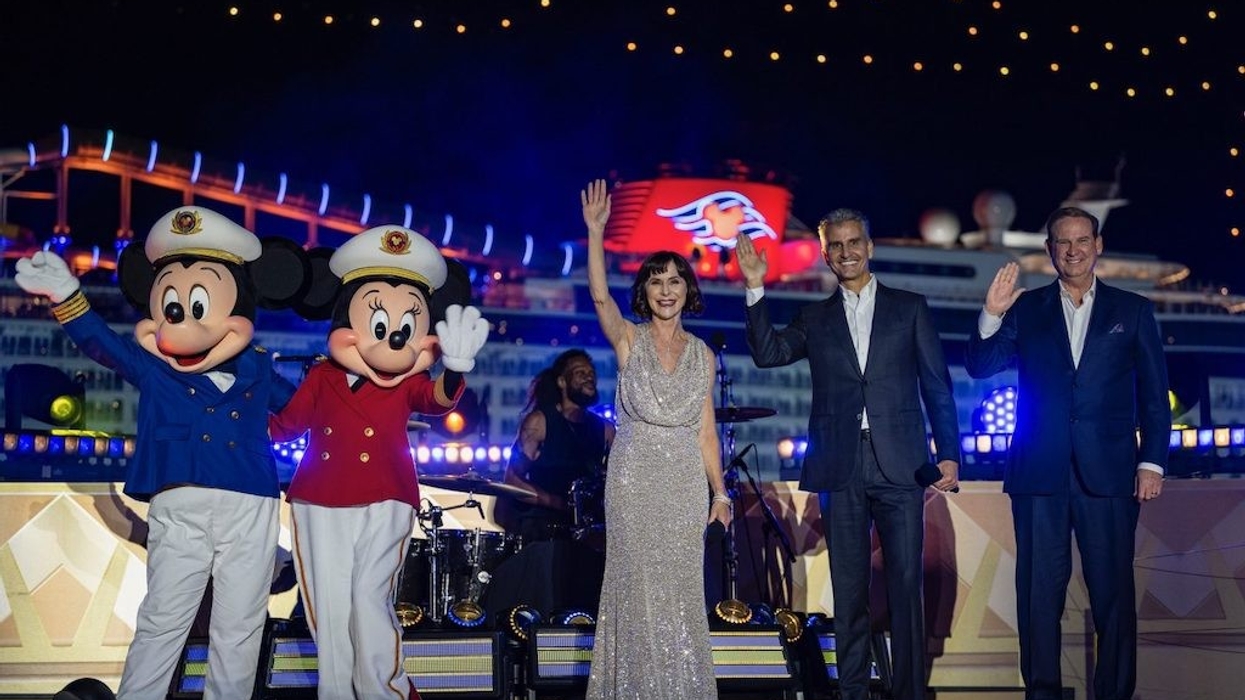 Performers and mascots wave on a brightly lit stage with a ship in the background.