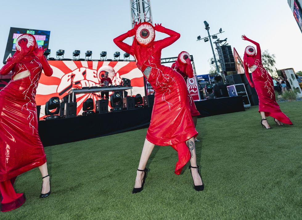 Performers in red costumes with eye motifs dance on a stage at Area15