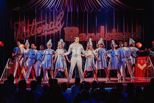 Performers in sparkly outfits on stage under "National Bandstand" sign.