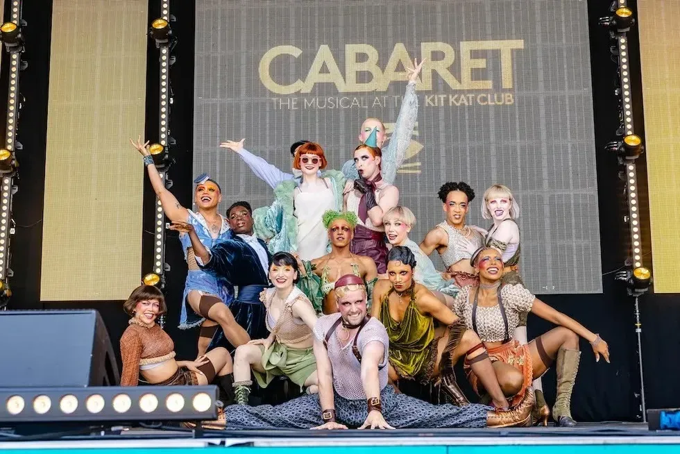 Performers in vibrant costumes pose on stage for "Cabaret" at Kit Kat Club.